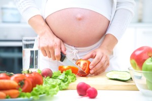Pregnant woman in kitchen making salad